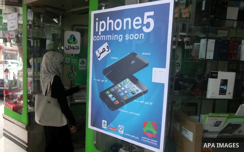 A Palestinian woman enters a mobile phone while display a portrait fo Apple's new iPhone 5 on the entrance, in Gaza City October 16, 2012. Apple's new iPhone 5 is selling well in the Gaza Strip despite inflated prices, r...