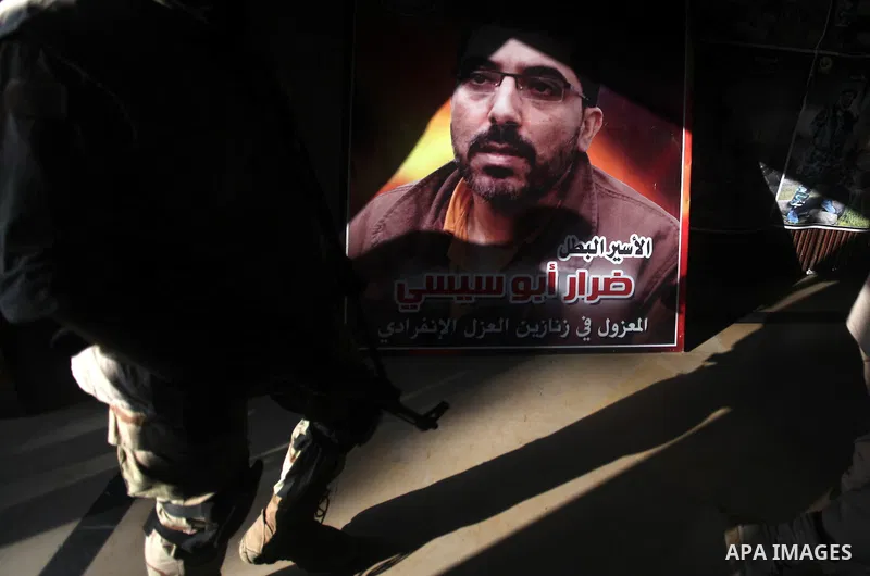 A Palestinian Hamas militant walks pass next to a portrait of a Palestinian prisoner during a ceremony to mark the first anniversary of a deal which saw the exchange of 1,027 Palestinian prisoners for captured Israeli so...