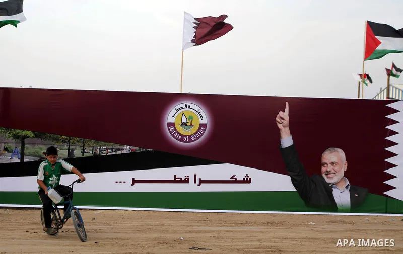 A Palestinian child rides his bicycle in front of the image of Palestinian Prime Minister in Gaza strip Ismail Haniyeh, adorn's a barrier where a project funded by Qatar is under construction, in Gaza City on October 21,...