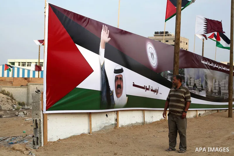 A Palestinian man looks at an image of the Emir of Qatar, Sheikh Hamad bin Khalifa Al-Thani, adorn's a barrier where a project funded by Qatar is under construction, in Gaza City on October 21, 2012. the day before the E...