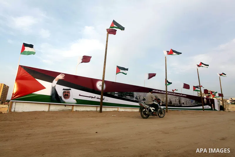 A Palestinian man rides his motorcycle in front of the image of the Emir of Qatar, Sheikh Hamad bin Khalifa Al-Thani, adorn's a barrier where a project funded by Qatar is under construction, in Gaza City on October 21, 2...