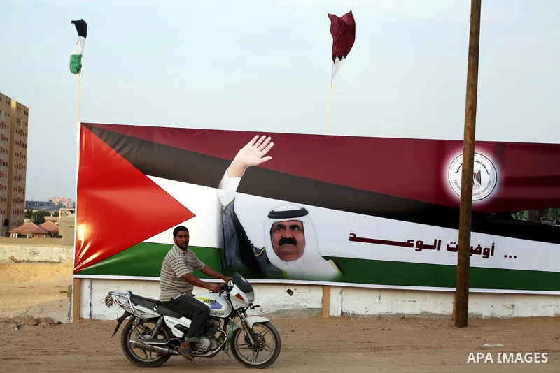 A Palestinian man rides his motorcycle in front of the image of the Emir of Qatar, Sheikh Hamad bin Khalifa Al-Thani, adorn's a barrier where a project funded by Qatar is under construction, in Gaza City on October 21, 2...
