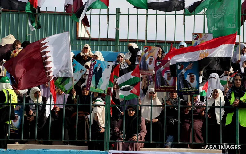 Palestinian Hamas supporters wave Qatari and Palestinian flags as others hold posters of the Emir of Qatar Sheikh Hamad bin Khalifa al-Thani, not pictured, as they wait for him to give a speech at the Palestine stadium i...