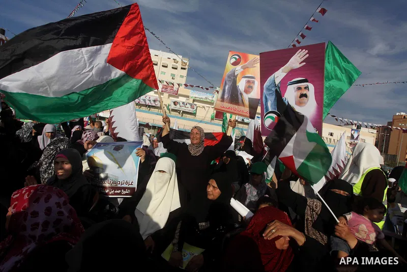Palestinian Hamas supporters wave Qatari and Palestinian flags as others hold posters of the Emir of Qatar Sheikh Hamad bin Khalifa al-Thani, not pictured, as they wait for him to give a speech at the Palestine stadium i...