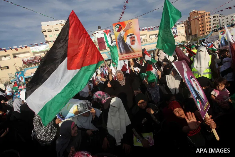 Palestinian Hamas supporters wave Qatari and Palestinian flags as others hold posters of the Emir of Qatar Sheikh Hamad bin Khalifa al-Thani, not pictured, as they wait for him to give a speech at the Palestine stadium i...
