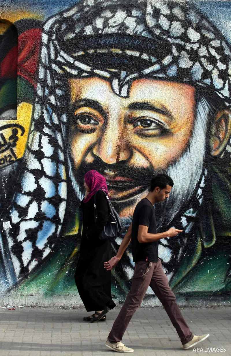 Palestinians passe by a mural depicting late Palestinian leader Yasser Arafat in Gaza City on Oct. 31, 2012. Palestinian authorities confirmed the November timetable to exhume the remains of former Palestinian leader Yas...