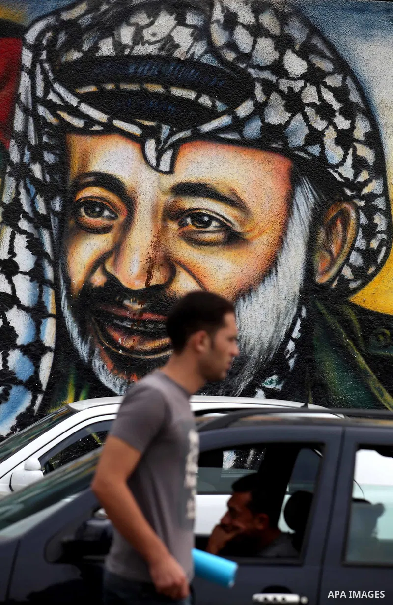 Palestinians passe by a mural depicting late Palestinian leader Yasser Arafat in Gaza City on Oct. 31, 2012. Palestinian authorities confirmed the November timetable to exhume the remains of former Palestinian leader Yas...