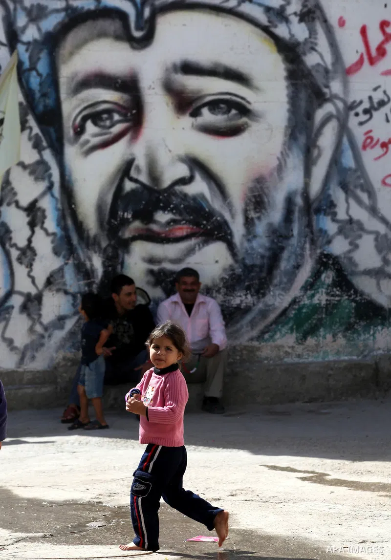 Palestinians sit in front of a mural of the Palestinian Leader Yasser Arafat in Gaza City, on November 10, 2012. "The Eighth anniversary of the departure of the founding leader". Photo by Majdi Fathi