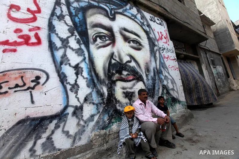 Palestinians sit in front of a mural of the Palestinian Leader Yasser Arafat in Gaza City, on November 10, 2012. "The Eighth anniversary of the departure of the founding leader". Photo by Majdi Fathi