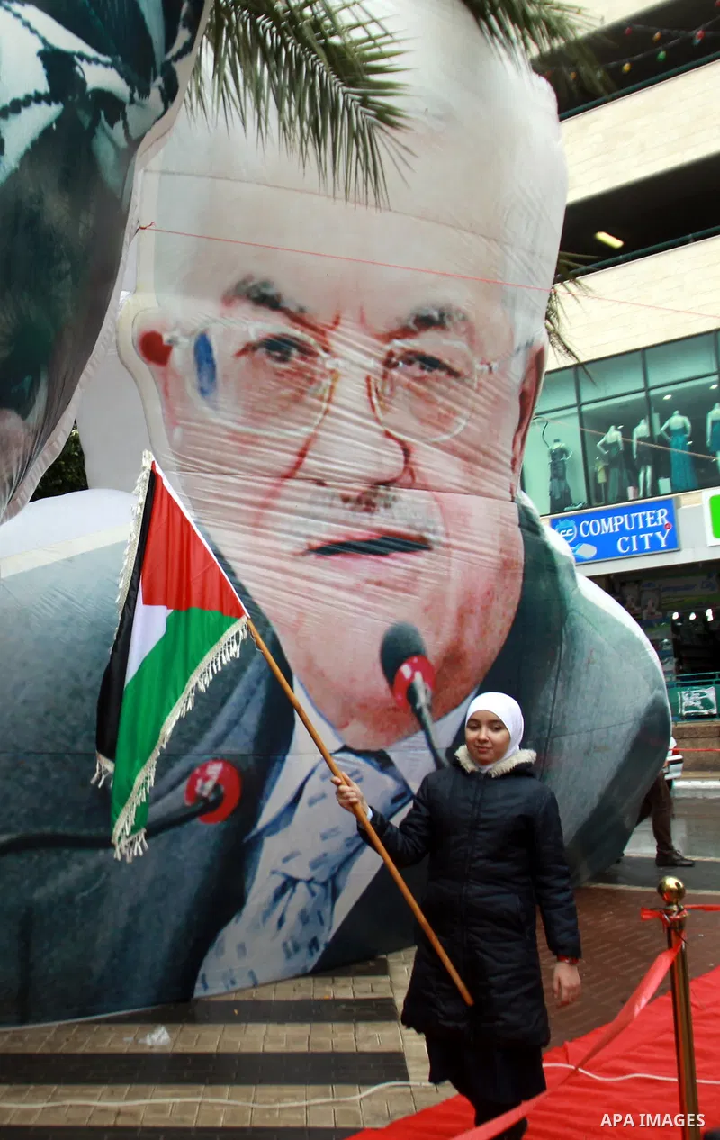 A Palestinian woman walks pass a mural of the late Yasser Arafat and current Palestinian President Mahmoud Abbas during the eighth anniversary of the death of the late leader Yasser Arafat, in the West Bank city of Nablu...