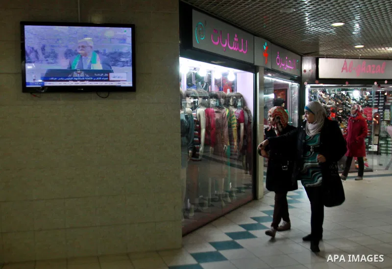 Palestinians walk at a shopping mall as Palestinian President Mahmud Abbas delivers a speech to mark the eighth anniversary of the death of the late leader Yasser Arafat, in the West Bank city of Nablus on November 11, 2...
