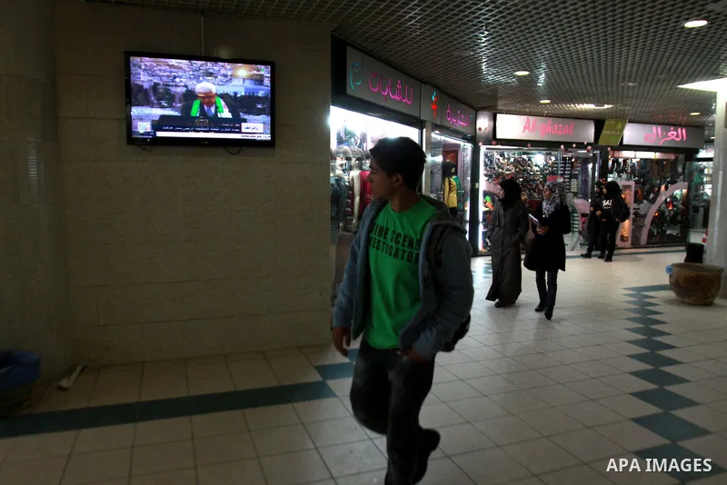 Palestinians walk at a shopping mall as Palestinian President Mahmud Abbas delivers a speech to mark the eighth anniversary of the death of the late leader Yasser Arafat, in the West Bank city of Nablus on November 11, 2...