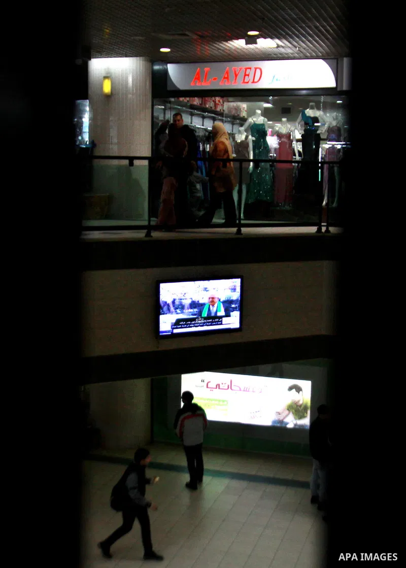 Palestinians walk at a shopping mall as Palestinian President Mahmud Abbas delivers a speech to mark the eighth anniversary of the death of the late leader Yasser Arafat, in the West Bank city of Nablus on November 11, 2...