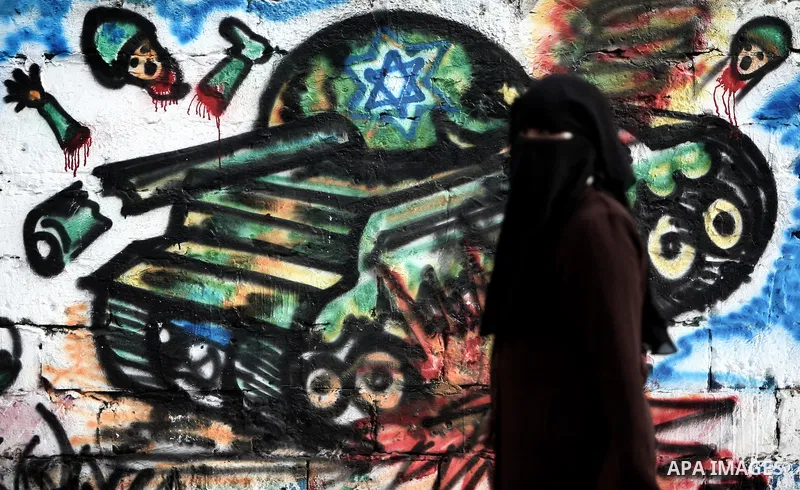 A Palestinian woman walks past a graffiti depicting a resistance fighter in Gaza City on November 12, 2012. The spike in violence, which comes as Israel is in the middle of an election campaign, raised the spectre of a b...