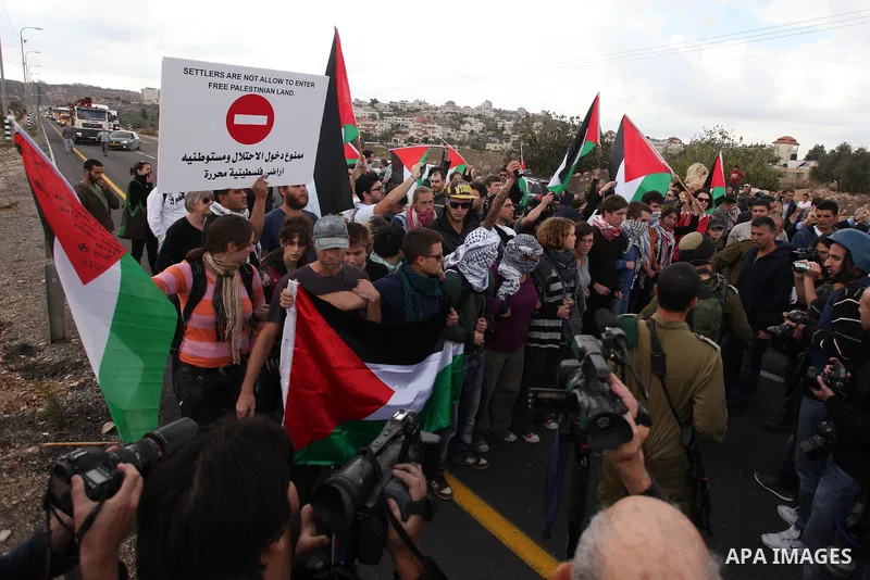 Palestinian and foreign activists hold placards reading "Settlers are not allow to enter free Palestinian land" and blocks a road leading to Ofra settlement near the West Bank city of Ramallah, on November 14, 2012, as P...