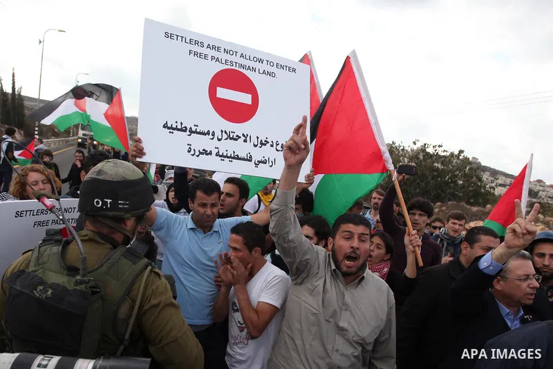 Palestinian and foreign activists hold placards reading "Settlers are not allow to enter free Palestinian land" and blocks a road leading to Ofra settlement near the West Bank city of Ramallah, on November 14, 2012, as P...