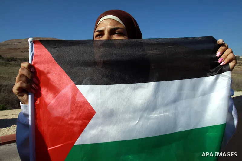 A Palestinian activist holds her national flag while she block a road leading to Huwwara checkpoint near the West Bank city of Nablus during a demonstration in support of the people of the Gaza Strip and against Israeli...