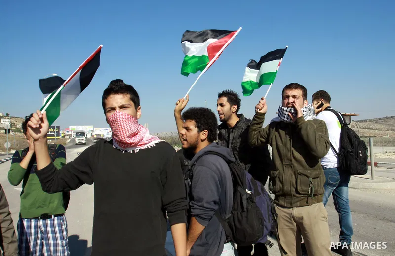 Palestinian activists hold their national flags while they block a road leading to Huwwara checkpoint near the West Bank city of Nablus during a demonstration in support of the people of the Gaza Strip and against Israel...