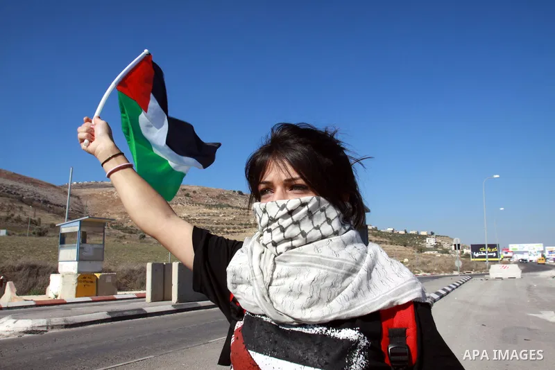 A Palestinian activist holds her national flag while she block a road leading to Huwwara checkpoint near the West Bank city of Nablus during a demonstration in support of the people of the Gaza Strip and against Israeli...