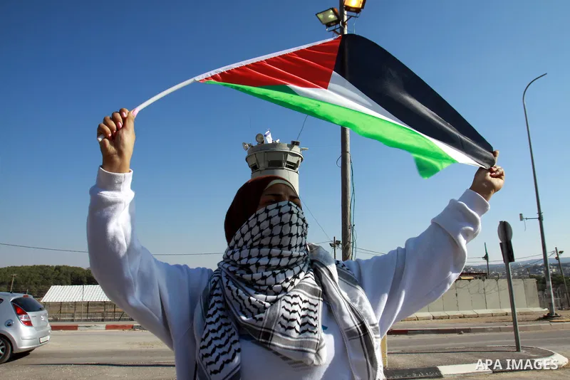 A Palestinian activist holds her national flag while she block a road leading to Huwwara checkpoint near the West Bank city of Nablus during a demonstration in support of the people of the Gaza Strip and against Israeli...