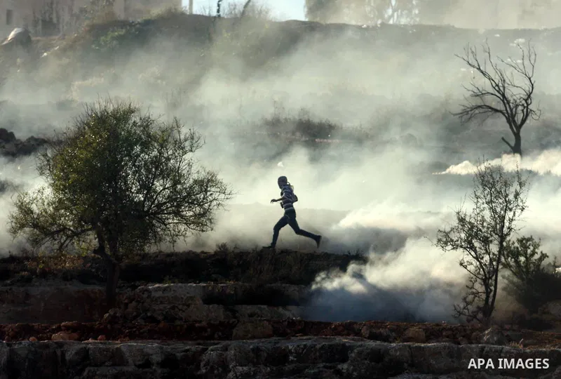 A Palestinian demonstrator runs through a cloud of tear gas during clashes against Israel's operations in Gaza Strip, outside Ofer, an Israeli military prison near the West Bank city of Ramallah, Thursday, Nov. 15, 2012....
