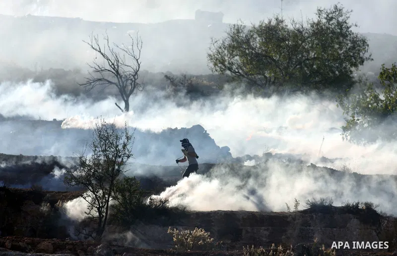 A Palestinian demonstrator runs through a cloud of tear gas during clashes against Israel's operations in Gaza Strip, outside Ofer, an Israeli military prison near the West Bank city of Ramallah, Thursday, Nov. 15, 2012....