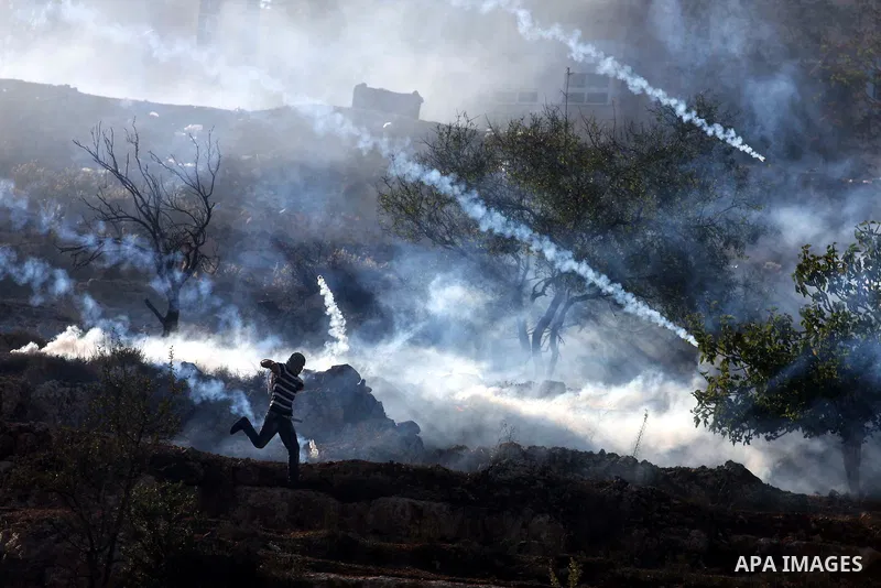 A Palestinian demonstrator runs through a cloud of tear gas during clashes against Israel's operations in Gaza Strip, outside Ofer, an Israeli military prison near the West Bank city of Ramallah, Thursday, Nov. 15, 2012....