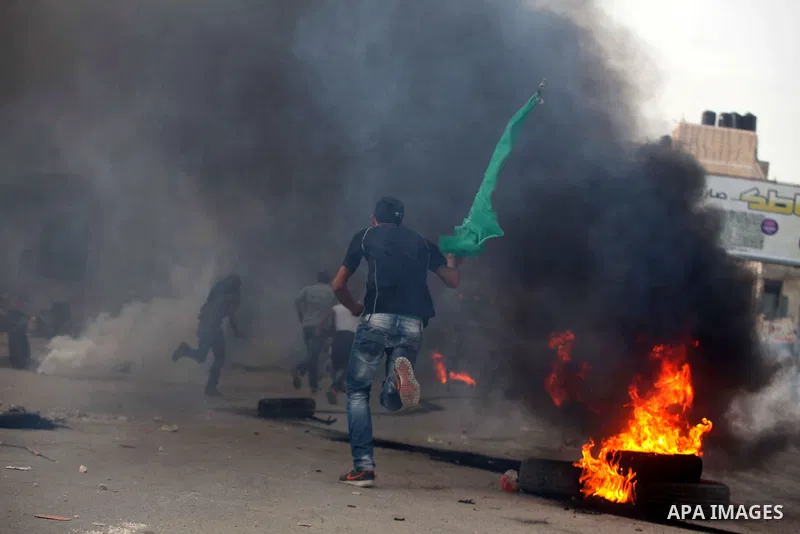 A Palestinian stone-thrower walks past smoke from burning tyres during clashes with Israeli security forces against Israel's military operation in Gaza, at Qalandia checkpoint near the West Bank city of Ramallah November...