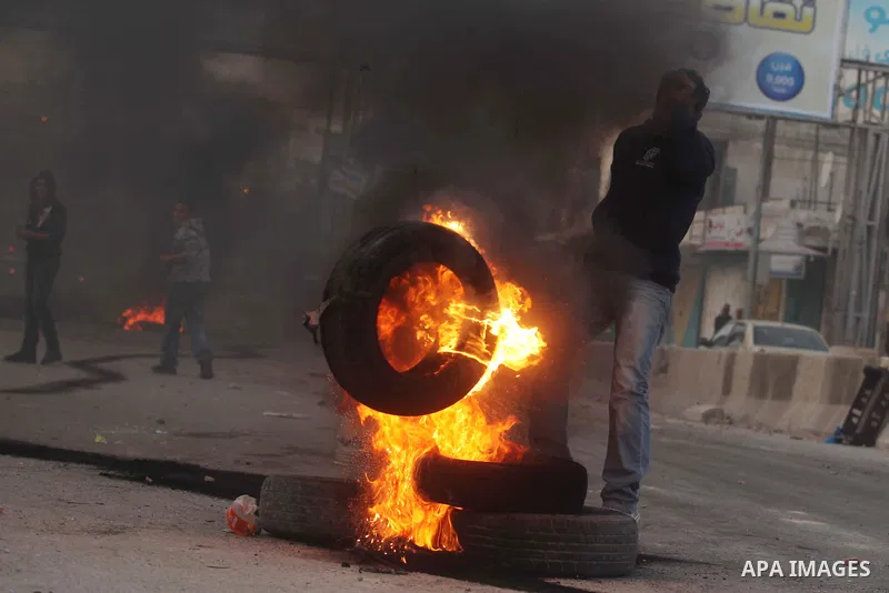 A Palestinian stone-thrower walks past smoke from burning tyres during clashes with Israeli security forces against Israel's military operation in Gaza, at Qalandia checkpoint near the West Bank city of Ramallah November...