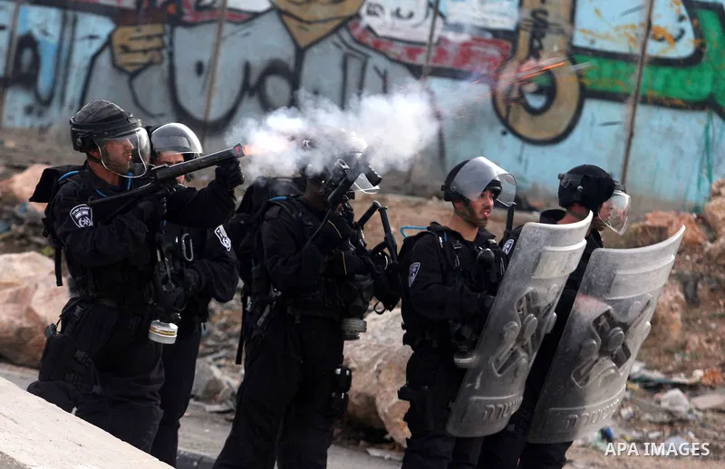 A Palestinian stone-thrower walks past smoke from burning tyres during clashes with Israeli security forces against Israel's military operation in Gaza, at Qalandia checkpoint near the West Bank city of Ramallah November...