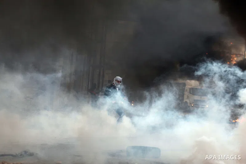 A Palestinian stone-thrower walks past smoke from burning tyres during clashes with Israeli security forces against Israel's military operation in Gaza, at Qalandia checkpoint near the West Bank city of Ramallah November...