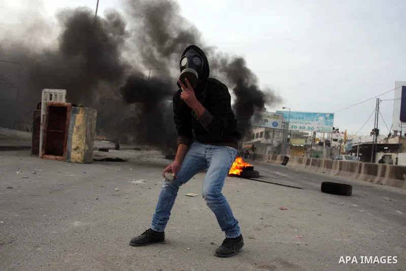 A Palestinian stone-thrower walks past smoke from burning tyres during clashes with Israeli security forces against Israel's military operation in Gaza, at Qalandia checkpoint near the West Bank city of Ramallah November...