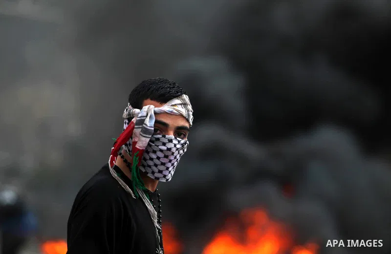 A Palestinian protester stands net a burned tire during clashes outside Ofer prison near the West Bank city of Ramallah November 18, 2012. The clashes broke out following a protest against Israel's military operation in...