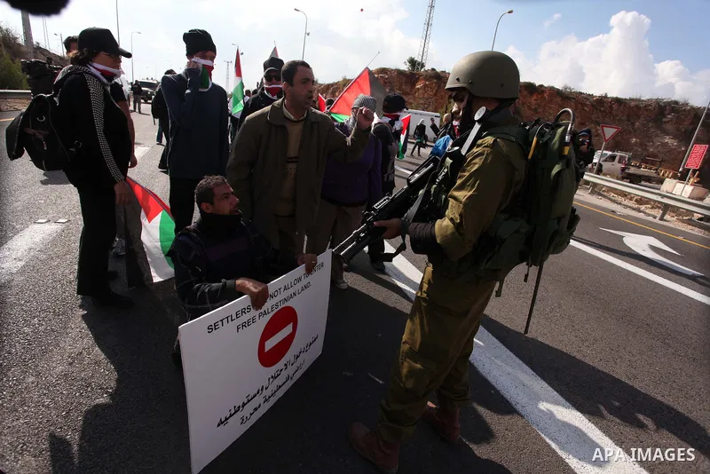 Israeli soldiers stand guard as Palestinian and foreign activists block the road between Ramallah and Nablus to protest against Israel's military action on the Gaza Strip, on November 19, 2012 in the West Bank village of...