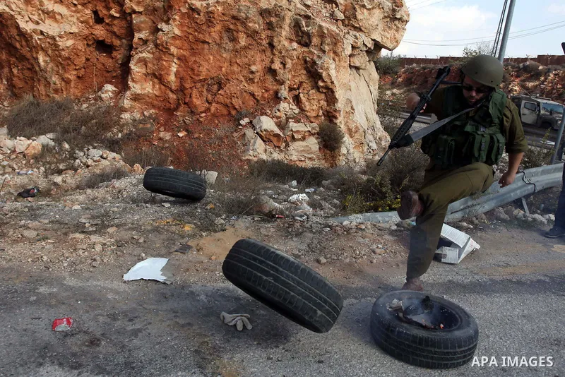 An Israeli soldier kicks a tire as Palestinian and foreign activists block the road between Ramallah and Nablus to protest against Israel's military action on the Gaza Strip, on November 19, 2012 in the West Bank village...
