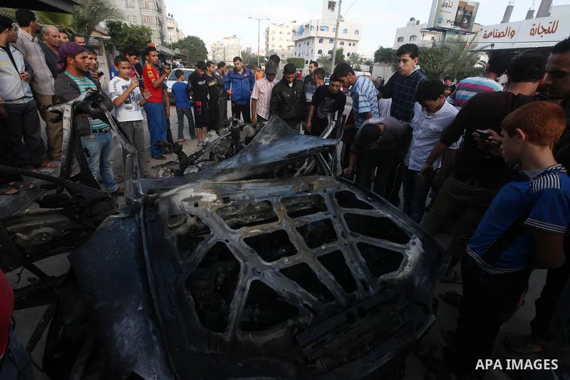Palestinians gather around a destroyed car which targeted by Israeli airstrike in the northen Gaza city, 19 November, 2012. Israeli aircraft killed A Palestinian and wounded two others in the raid. Media reports that Isr...