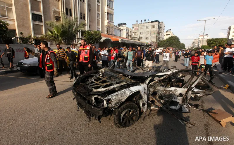Palestinians gather around a destroyed car which targeted by Israeli airstrike in the northen Gaza city, 19 November, 2012. Israeli aircraft killed A Palestinian and wounded two others in the raid. Media reports that Isr...