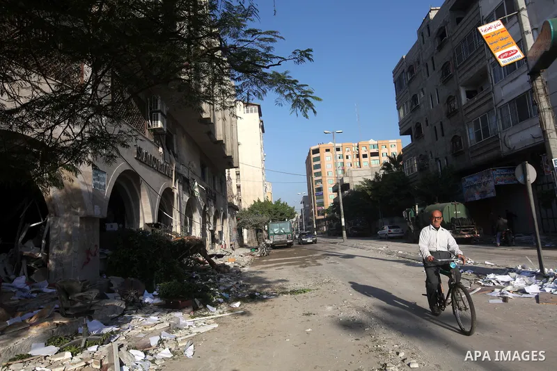 A Palestinian man rides his bicycle in front of the damage after an Israeli air strike on the Islamic National Bank building in Gaza City on November 20, 2012. Israeli leaders discussed an Egyptian plan for a truce with...