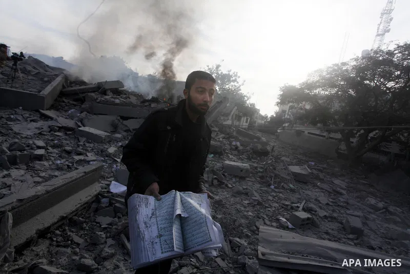 A Palestinian man carry a copy of the holy Quraan at government offices destroyed in an Israeli airstrike in Gaza City, 21 November 2012. Palestinian militants renewed their rocket fire on Israel 21 November and Israel c...