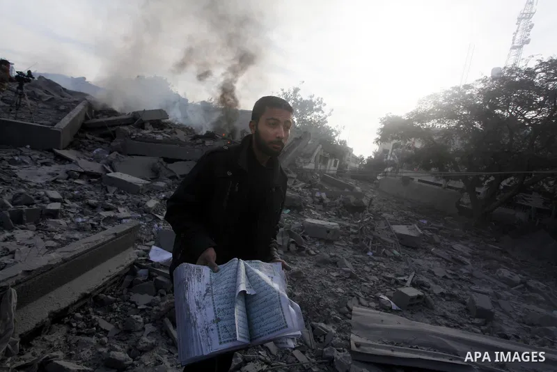 A Palestinian man carry a copy of the holy Quraan at government offices destroyed in an Israeli airstrike in Gaza City, 21 November 2012. Palestinian militants renewed their rocket fire on Israel 21 November and Israel c...