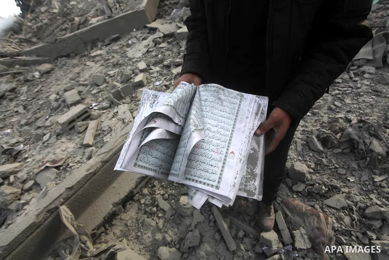 A Palestinian man carry a copy of the holy Quraan at government offices destroyed in an Israeli airstrike in Gaza City, 21 November 2012. Palestinian militants renewed their rocket fire on Israel 21 November and Israel c...