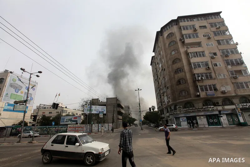 Palestinians look at smoke as rises from a building in an Israeli airstrike in Gaza City, 21 November 2012. Palestinian militants renewed their rocket fire on Israel 21 November and Israel continued pounding targets in t...