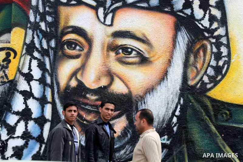 Palestinians walk in front of a mural of late Palestinian leader Yasser Arafat in Gaza City on November 27, 2012. The body of Arafat was exhumed, eight years after his death, as part of an investigation into allegations...