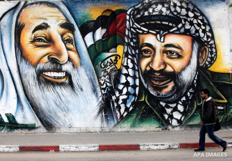 Palestinians walk in front of a mural of late Palestinian leader Yasser Arafat in Gaza City on November 27, 2012. The body of Arafat was exhumed, eight years after his death, as part of an investigation into allegations...