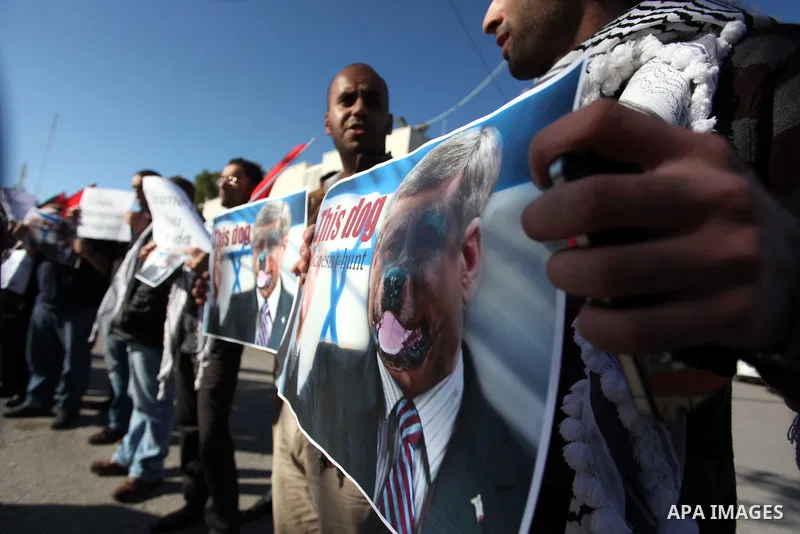 Palestinians hold national flags and a poster of Canadian Prime Minister Stephen Harper superimposed with a face of a dog during a protest following his remarks about the Palestinian UN bid for an observer state status,...