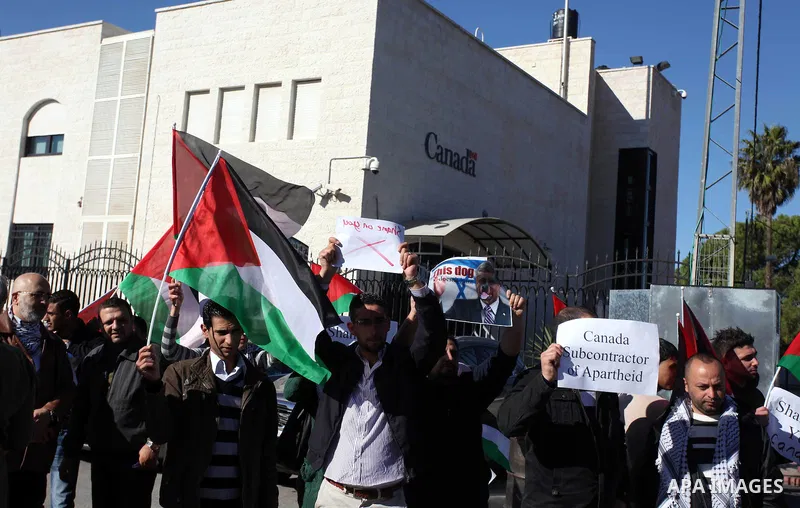 Palestinians hold national flags and a poster of Canadian Prime Minister Stephen Harper superimposed with a face of a dog during a protest following his remarks about the Palestinian UN bid for an observer state status,...