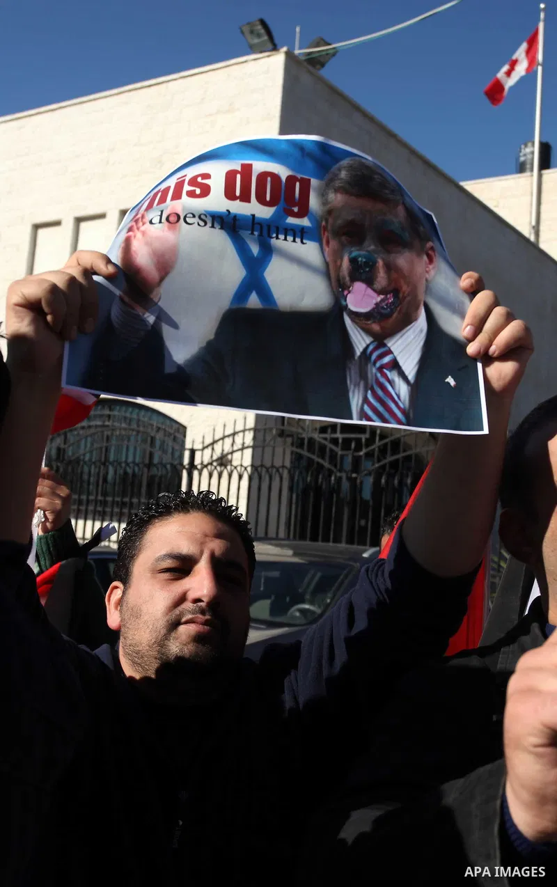 Palestinians hold national flags and a poster of Canadian Prime Minister Stephen Harper superimposed with a face of a dog during a protest following his remarks about the Palestinian UN bid for an observer state status,...