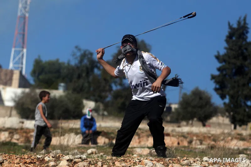 A Palestinian protester hurls a stone at Israeli security forces during a protest against the expansion of the nearby Jewish settlement of Halamish, in the West Bank village of Nabi Saleh near Ramallah, Friday, Nov. 30,...
