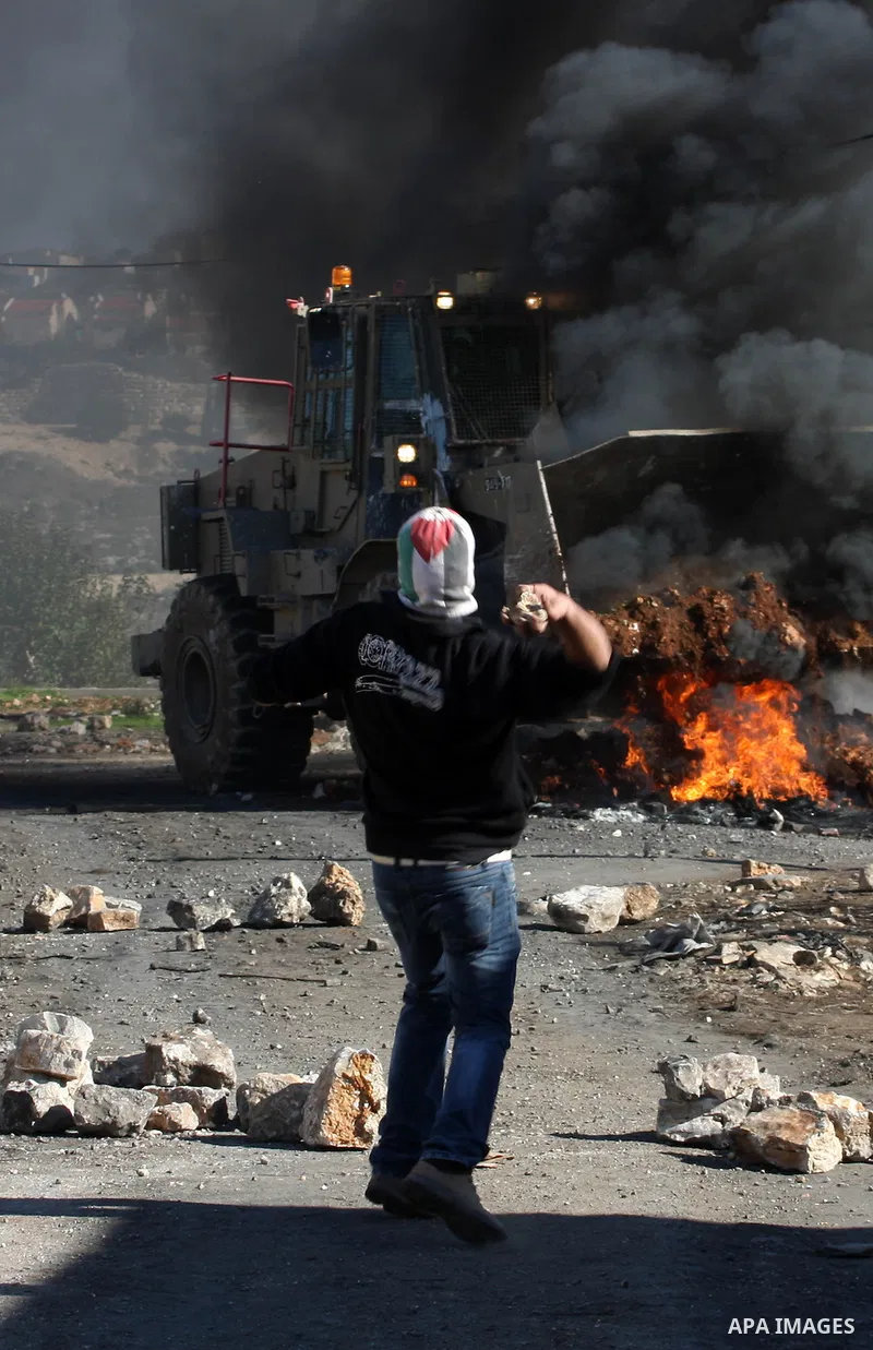 A Palestinian protester throws stones at Israeli bulldozer on the sidelines of a demonstration against the expropriations by Israel in the West Bank village of Kafr Qaddum, near Nablus, on November 30, 2012. Photo by Ned...