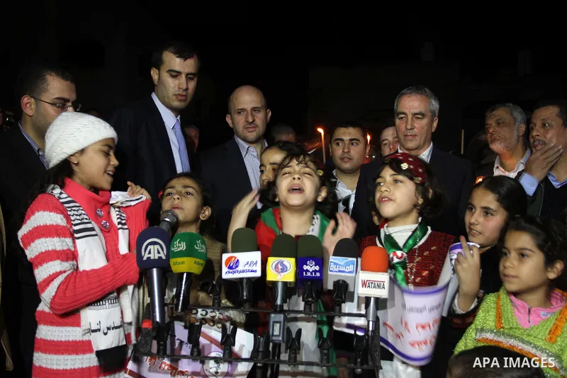 Palestinian childrens speak during a solidarity march with the Dalu family next to their house, as well as a wrecked car festooned with candles, which was hit by an Israeli strike during Israel's recent military offensiv...